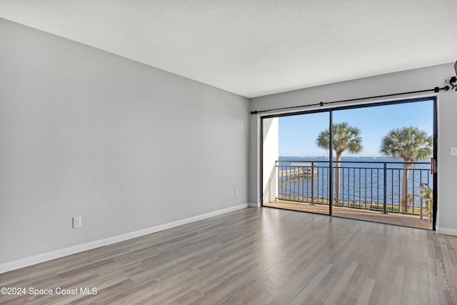 unfurnished room with hardwood / wood-style floors, a water view, and a textured ceiling