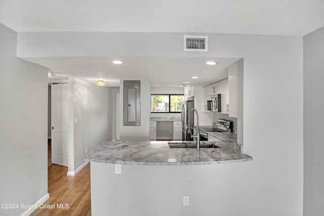 kitchen with white cabinets, light wood-type flooring, a textured ceiling, kitchen peninsula, and stainless steel appliances