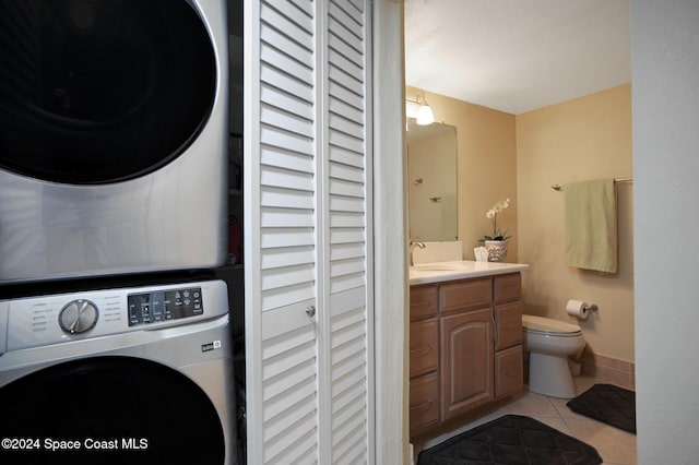 clothes washing area featuring sink, light tile patterned floors, and stacked washer / dryer