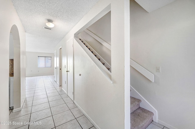 hallway with a textured ceiling and light tile patterned flooring