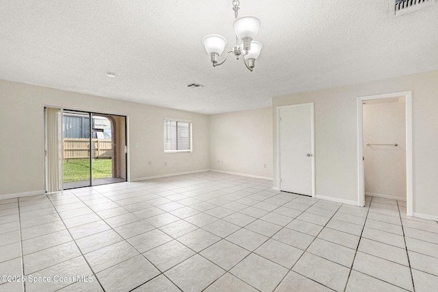 empty room featuring light tile patterned floors, a textured ceiling, and a notable chandelier