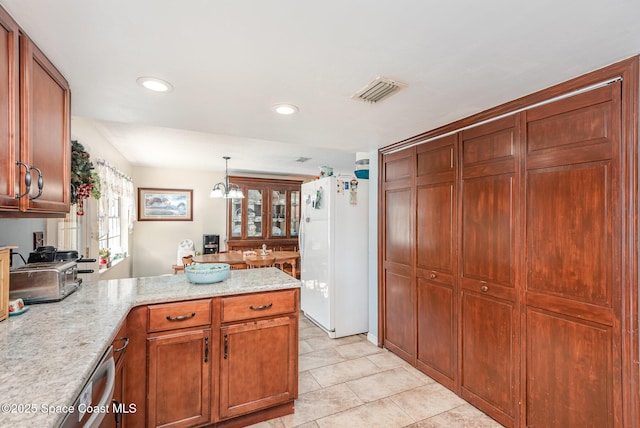 kitchen with light tile patterned flooring, hanging light fixtures, light stone countertops, white fridge, and kitchen peninsula