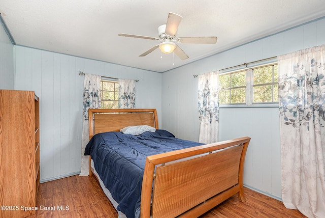 bedroom with ceiling fan, wood walls, and hardwood / wood-style flooring