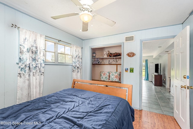 bedroom with wood-type flooring, a closet, ceiling fan, and wood walls