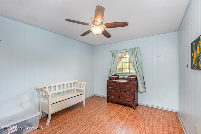 bedroom with ceiling fan, wooden walls, and light hardwood / wood-style floors