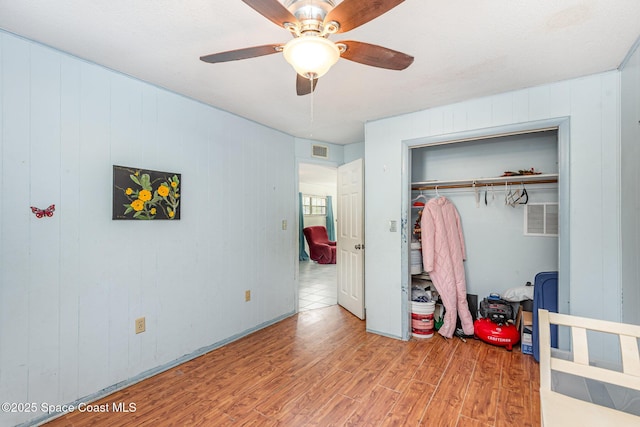 bedroom featuring ceiling fan, a closet, wood walls, and light hardwood / wood-style flooring