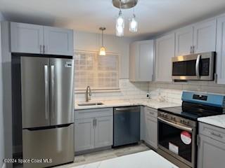 kitchen with gray cabinetry, hanging light fixtures, sink, decorative backsplash, and appliances with stainless steel finishes