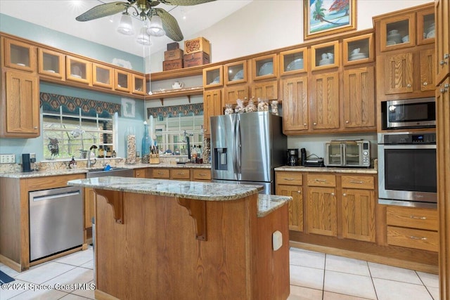 kitchen featuring light stone countertops, appliances with stainless steel finishes, light tile patterned floors, and a kitchen island