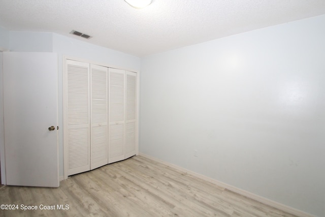 unfurnished bedroom featuring a textured ceiling, light hardwood / wood-style flooring, and a closet