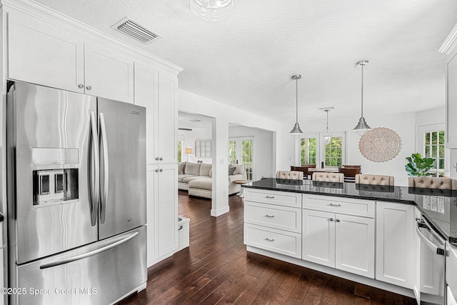 kitchen featuring white cabinets, dark stone countertops, hanging light fixtures, and appliances with stainless steel finishes