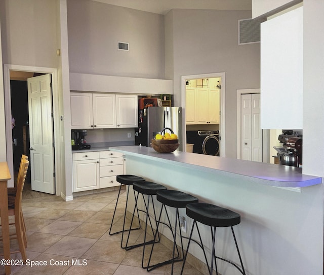 kitchen with stainless steel refrigerator with ice dispenser, a kitchen bar, kitchen peninsula, white cabinets, and a high ceiling