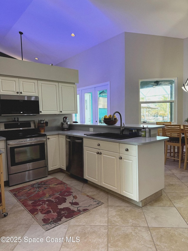 kitchen featuring appliances with stainless steel finishes, white cabinetry, sink, light tile patterned floors, and kitchen peninsula