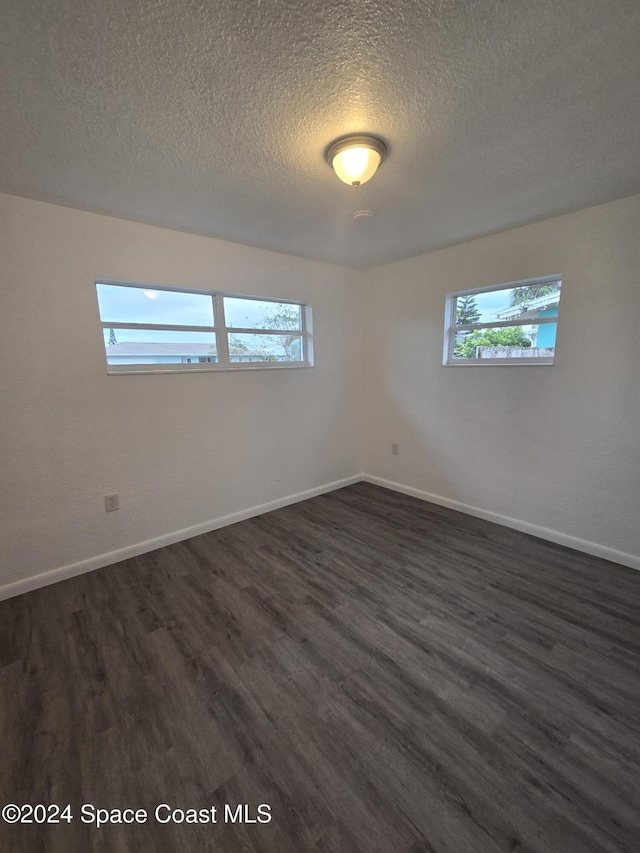 spare room featuring a textured ceiling, a healthy amount of sunlight, and dark hardwood / wood-style floors