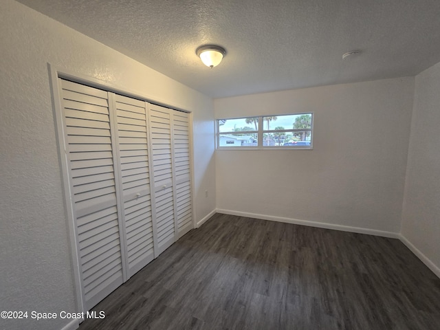 unfurnished bedroom featuring a textured ceiling, dark hardwood / wood-style flooring, and a closet