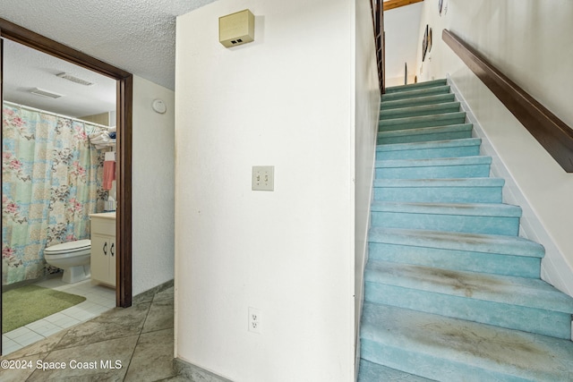 stairway with a textured ceiling and tile patterned floors