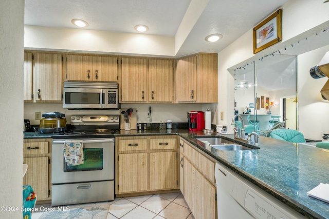 kitchen featuring sink, dark stone countertops, a textured ceiling, appliances with stainless steel finishes, and light tile patterned flooring