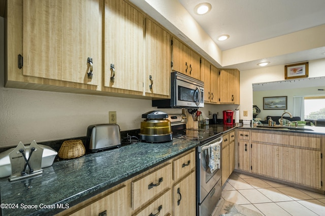 kitchen with light tile patterned flooring, stainless steel appliances, dark stone counters, and sink