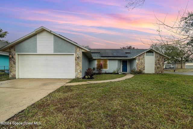 ranch-style house with a yard, a garage, and solar panels