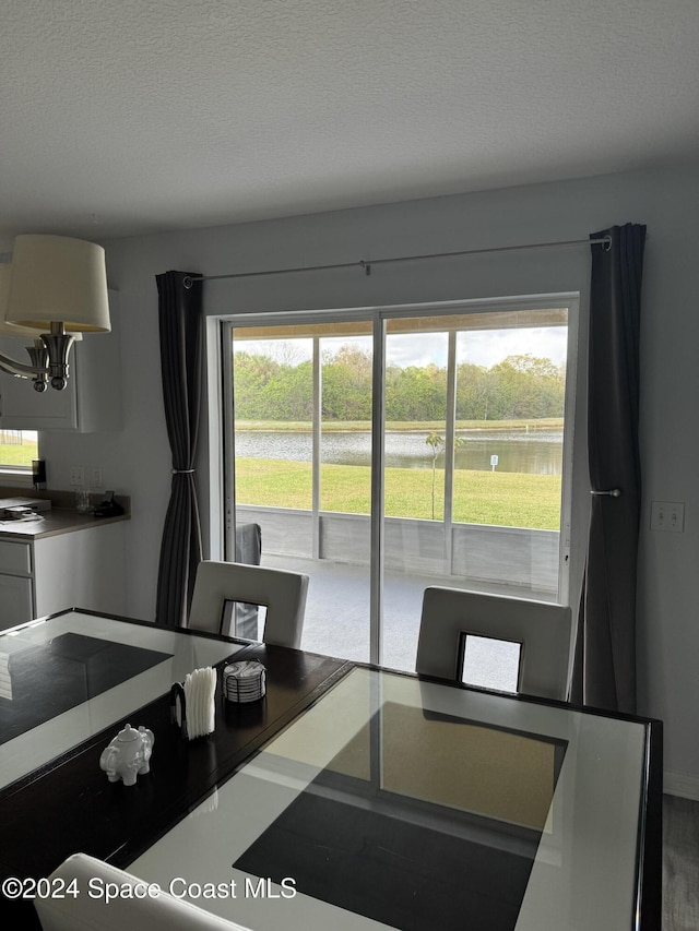 dining room featuring a water view, wood-type flooring, a textured ceiling, and a wealth of natural light