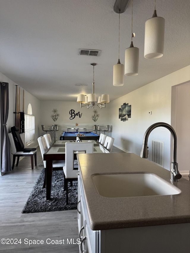 kitchen featuring white cabinetry, sink, hanging light fixtures, light hardwood / wood-style flooring, and a center island with sink