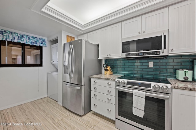 kitchen with stacked washing maching and dryer, tasteful backsplash, light stone counters, white cabinets, and appliances with stainless steel finishes