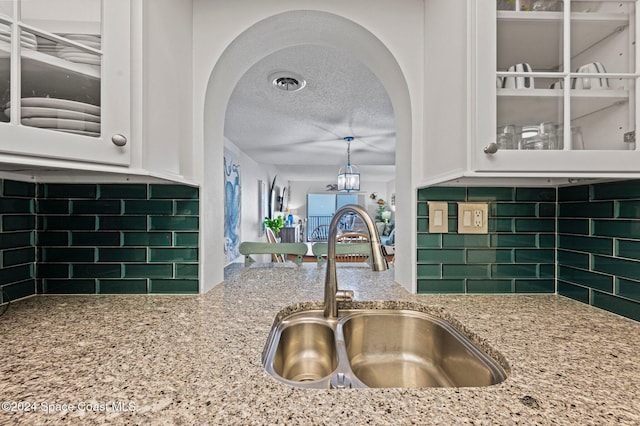 kitchen featuring a textured ceiling, backsplash, white cabinetry, and sink