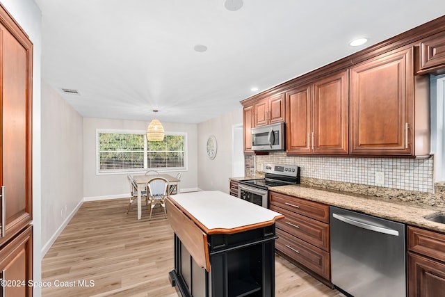 kitchen with a center island, stainless steel appliances, light stone counters, backsplash, and light hardwood / wood-style floors