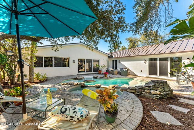 401 S Palm Ave, Indialantic, FL 32903 - back of property featuring stucco siding, a patio area, a metal roof, an outdoor hangout area, and a pool with connected hot tub
