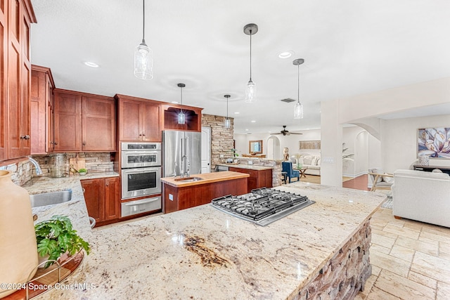 kitchen with light stone countertops, ceiling fan, stainless steel appliances, decorative light fixtures, and a kitchen island