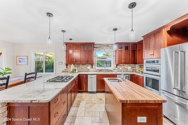 kitchen with a wealth of natural light, an island with sink, stainless steel appliances, and decorative light fixtures