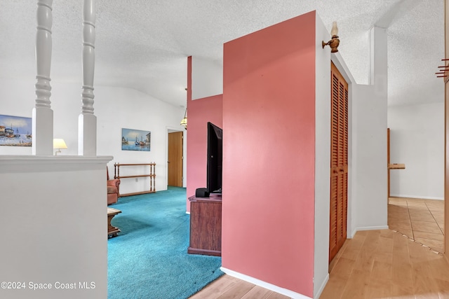 corridor with hardwood / wood-style floors, a textured ceiling, and vaulted ceiling