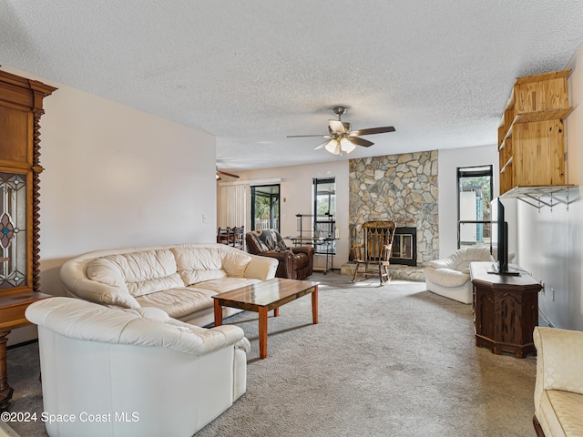 carpeted living room featuring a textured ceiling, a stone fireplace, and ceiling fan