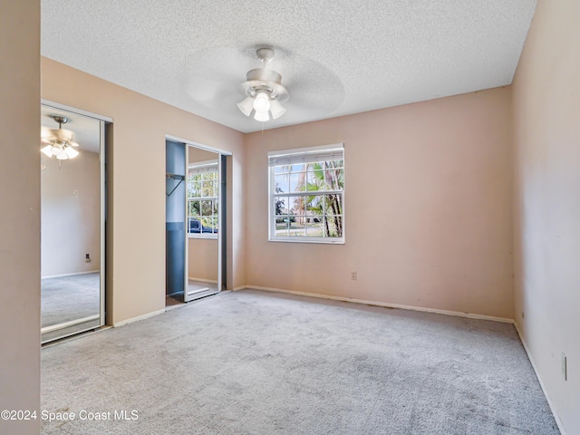 empty room with ceiling fan, light colored carpet, and a textured ceiling