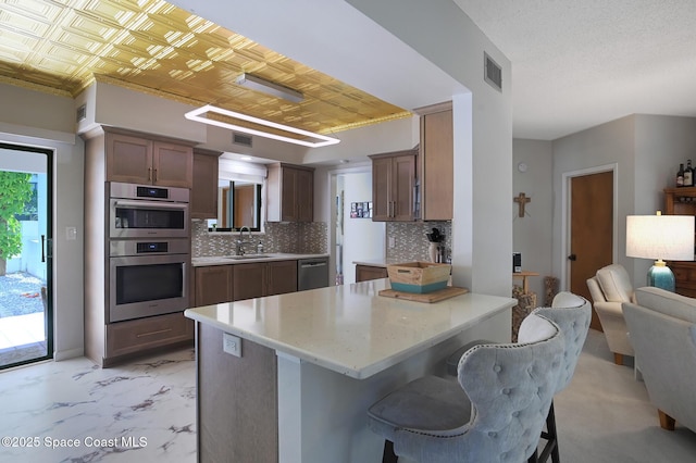 kitchen with appliances with stainless steel finishes, decorative backsplash, sink, a kitchen bar, and kitchen peninsula