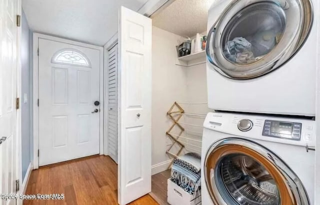 clothes washing area with stacked washer and dryer, a textured ceiling, and light hardwood / wood-style flooring