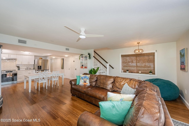 living area featuring visible vents, ceiling fan, stairway, and wood finished floors