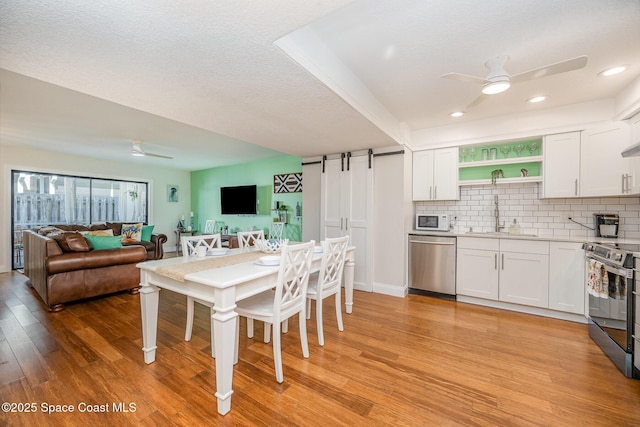 dining area featuring ceiling fan, sink, light hardwood / wood-style flooring, and a barn door