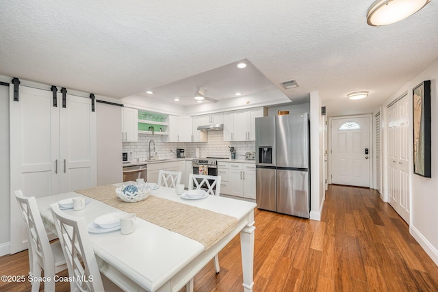 kitchen with a barn door, white cabinetry, light countertops, appliances with stainless steel finishes, and open shelves