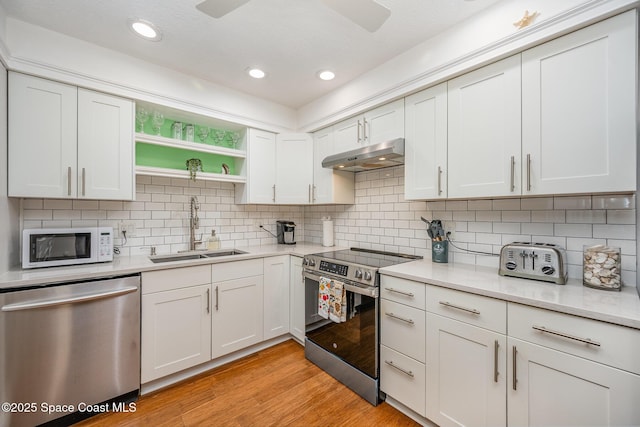 kitchen with appliances with stainless steel finishes, backsplash, white cabinets, light hardwood / wood-style flooring, and sink