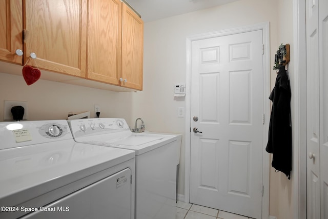 clothes washing area featuring washer and dryer, light tile patterned flooring, and cabinets