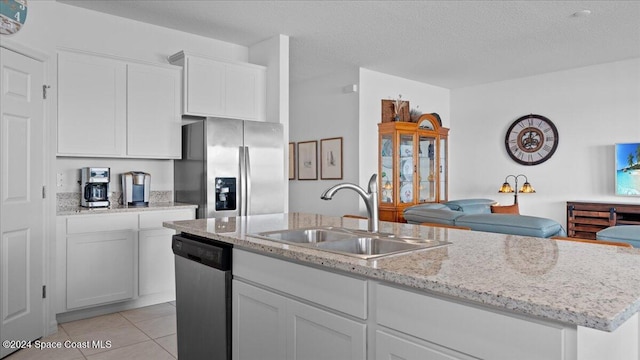 kitchen with sink, light tile patterned floors, stainless steel appliances, a kitchen island with sink, and white cabinets