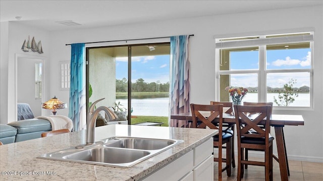 kitchen with a water view, white cabinetry, sink, and light tile patterned floors