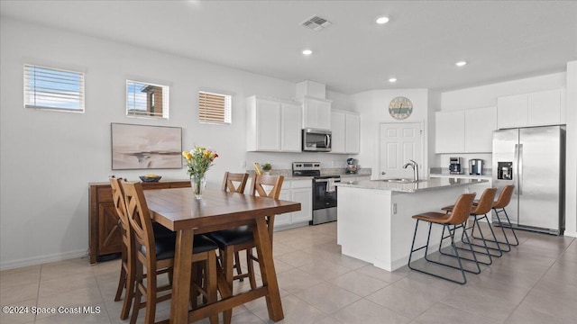 kitchen featuring a breakfast bar, an island with sink, white cabinetry, stainless steel appliances, and light stone countertops