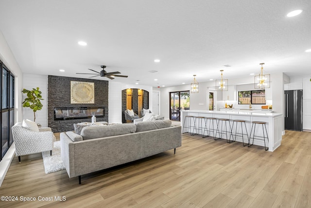 living room with ceiling fan, sink, light hardwood / wood-style floors, a textured ceiling, and a fireplace