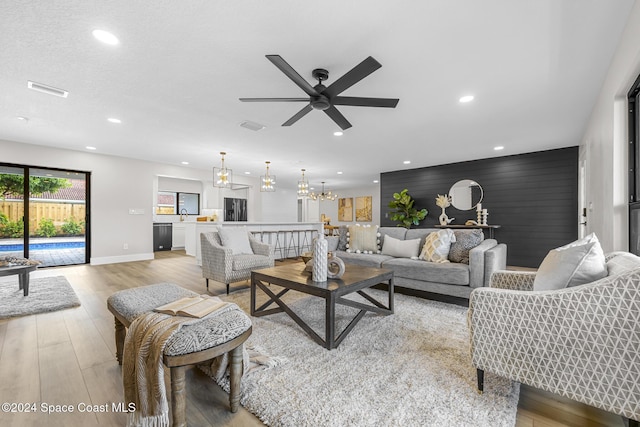 living room featuring ceiling fan with notable chandelier and light wood-type flooring