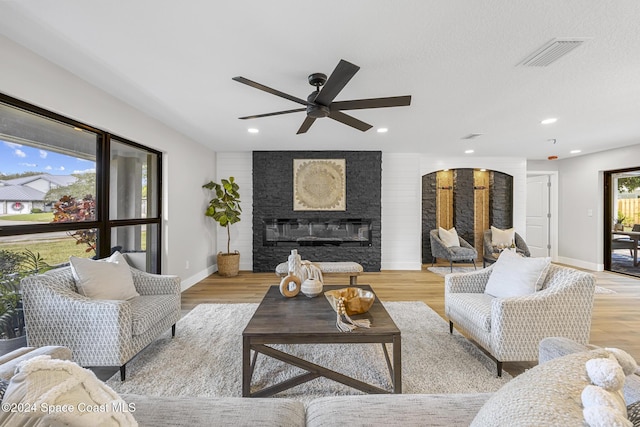 living room featuring a large fireplace, ceiling fan, and light hardwood / wood-style flooring