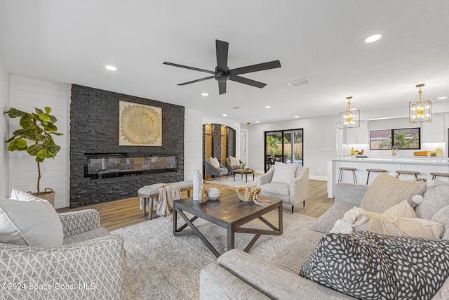 living room with ceiling fan with notable chandelier, light hardwood / wood-style floors, and a stone fireplace