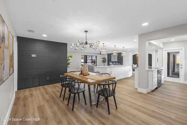 dining area with light hardwood / wood-style floors, a textured ceiling, and a notable chandelier