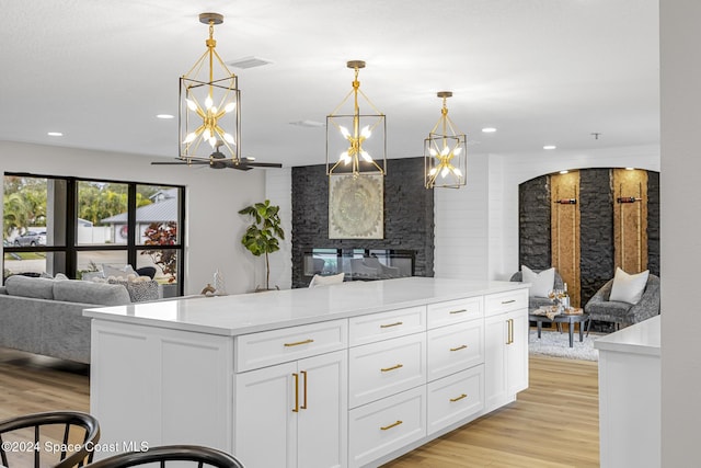 kitchen featuring a stone fireplace, white cabinetry, decorative light fixtures, and light wood-type flooring