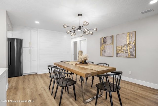 dining room featuring wood walls, a notable chandelier, light hardwood / wood-style floors, and a textured ceiling